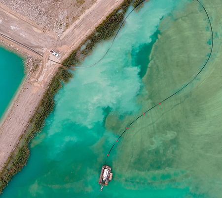 Aerial drone view of colorful turquoise blue mining tailings with vehicles and boat