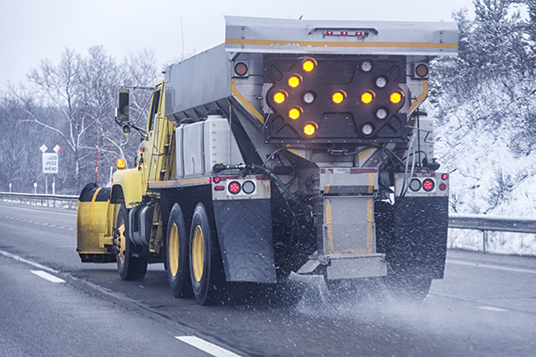 A snowplow scatters road salt on a highway during winter. Road salt—typically sodium chloride—helps keep winter roads, sidewalks, and parking lots safe, but it can also enter the environment during storage, transport, or application.