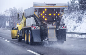 A snowplow scatters road salt on a highway during winter. Road salt—typically sodium chloride—helps keep winter roads, sidewalks, and parking lots safe, but it can also enter the environment during storage, transport, or application.