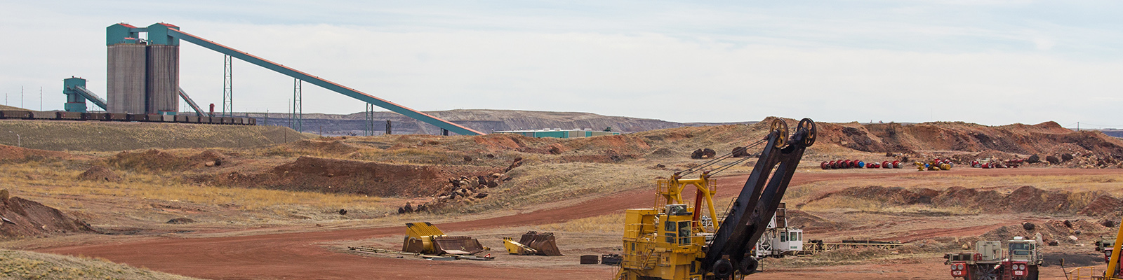 Industrial coal mining equipment and silos beside a row of railway cars in a Wyoming valley landscape.