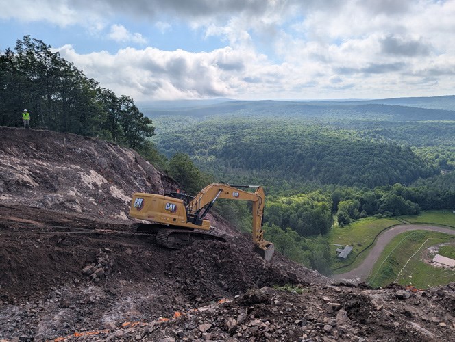 An excavator shapes the massive landing hill of the Copper Peak ski jump against a forest background.