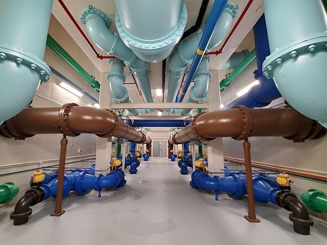 A room filled with large blue, brown, and green industrial pipes runs in parallel rows along the floor and ceiling.