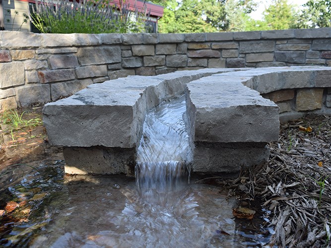 A narrow stone channel in a spiral shape sending stormwater into a raingarden.
