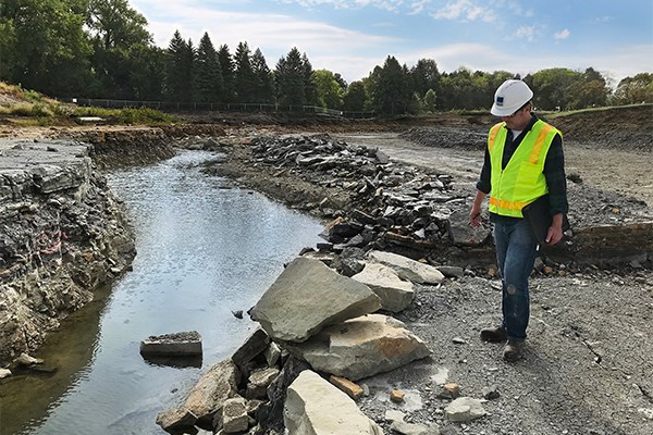 A man stands next to an engineered creek channel with flowing water at a construction site.