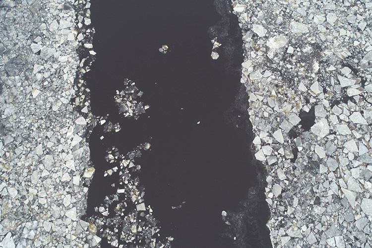 A dark channel of open water runs between dense fields of broken, floating ice fragments.