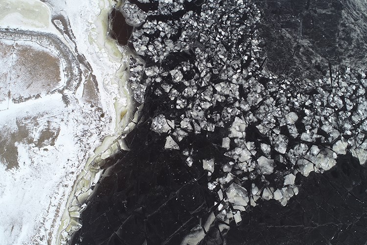 A jagged boundary of broken ice meets dark frozen water beside a snow‑covered shoreline.