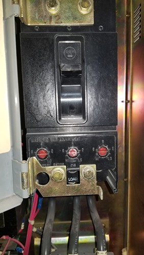 Close-up of an electrical circuit breaker with a black ON/OFF switch, three red magnetic trip adjustment dials labeled 2 to 10, and wires connected at the bottom marked ‘LOAD.’