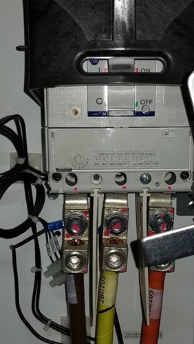 Electrical circuit breaker panel with a switch in the OFF position and three thick color-coded cables—brown, yellow, and orange—secured to terminals at the bottom.